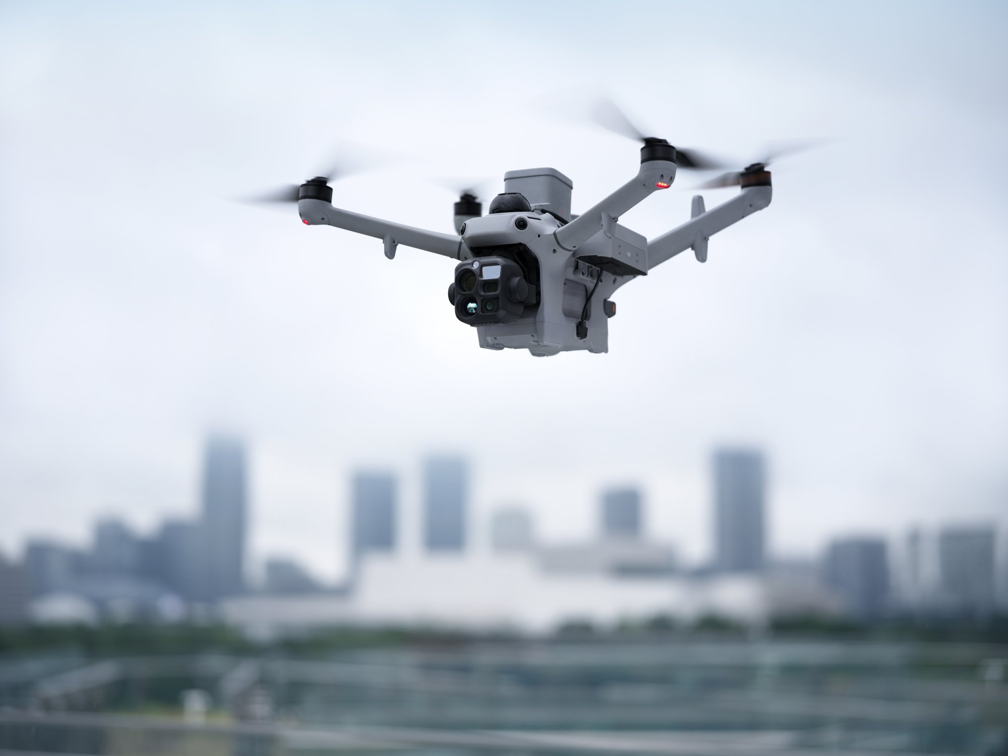 DJI Matrice 5TD su garsiakalbiu ir prožektoriumi mieste